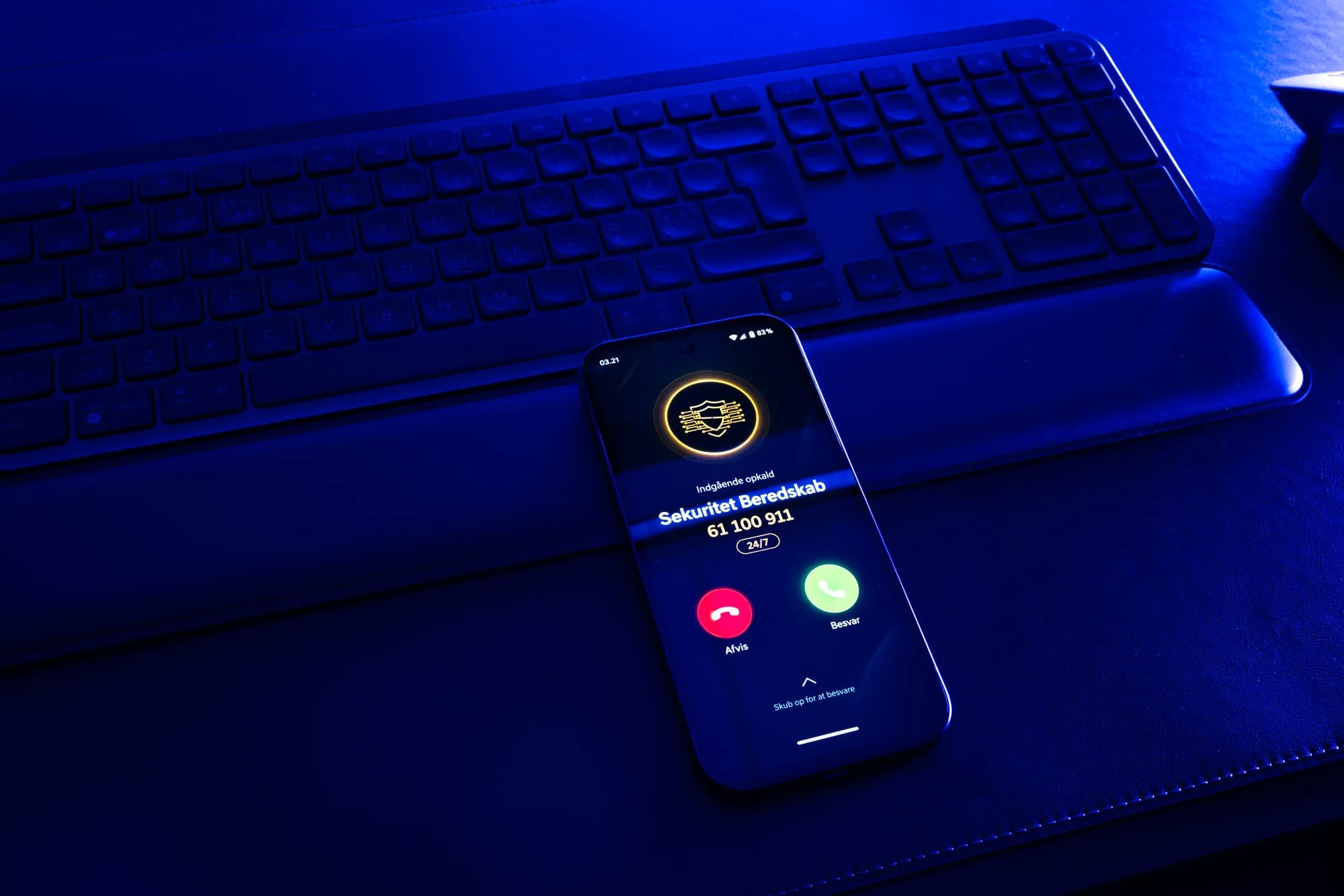 Telefon ligger på et tastatur i blåt lys og viser et indgående opkald fra Sekuritet Beredskab, 61 100 911